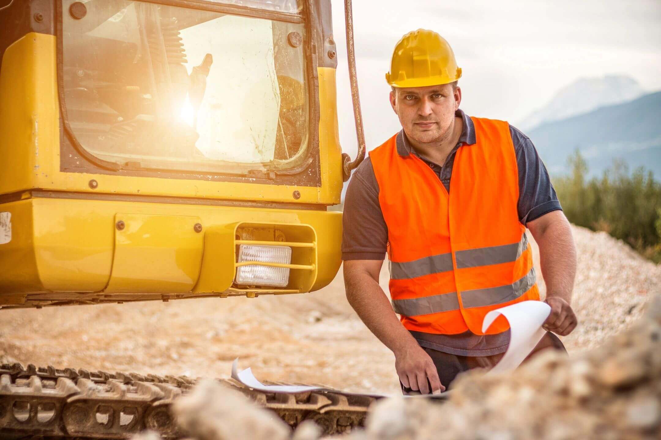 Construction worker in safety gear inspecting rubble at a site.